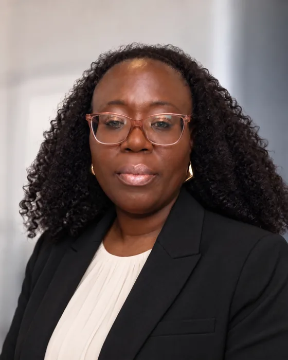 Dr. Aminata Kanu, founder of RESSETT LAB, in a black blazer, cream blouse and pink-framed glasses